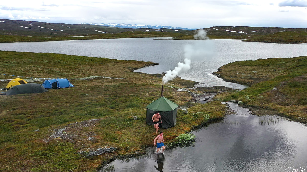 Tältbastu vid en fjällsjö där två personer springer ner till vattnet för att svalka sig